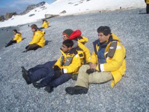 People sitting on rocky Antarctic beach with penguins and abandoned boat in background