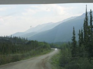 Caravan driving through forest with mountains in background